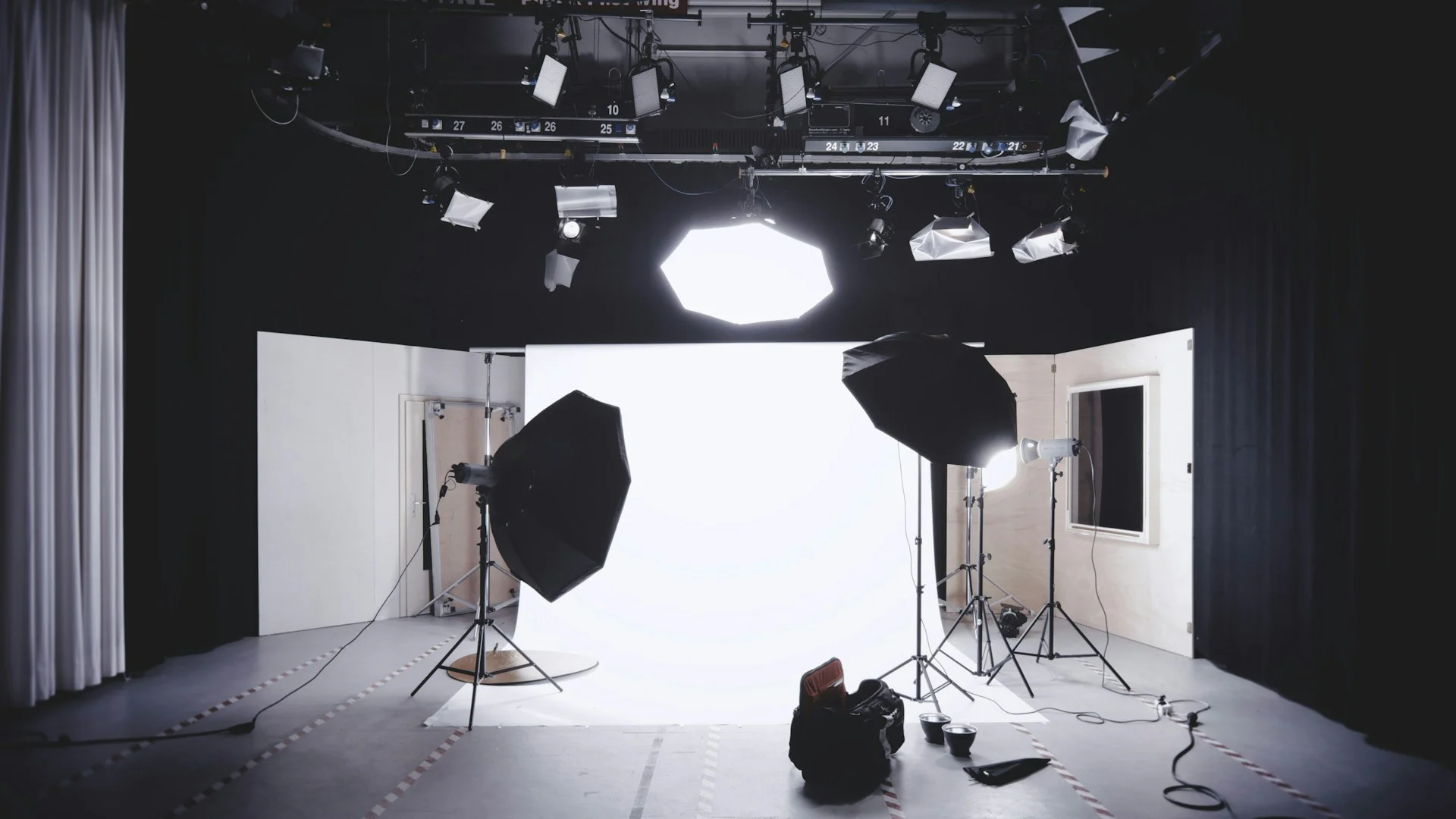 Fotografické studio s bílým pozadím, softboxy na stativech a světly na stropní rampě